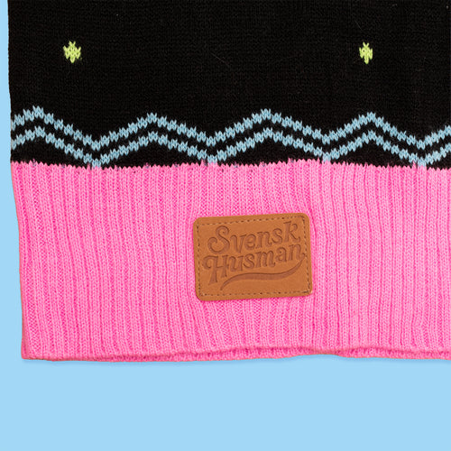 Närbild på jultröja med rosa ribbad mudd, blått sicksackmönster och läderlogo från Svenskhusman.