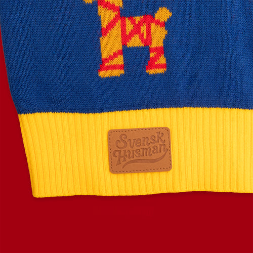 Blå stickad jultröja med gul mudd och brun läderpatch från Svenskhusman på röd bakgrund.