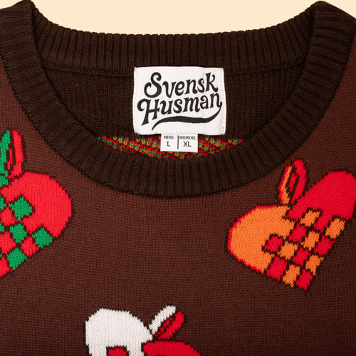 Brun stickad jultröja med färgglada julhjärtan och vit nacketikett med Svenskhusman-logotyp.