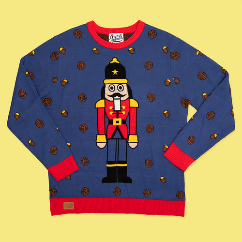 Blå stickad jultröja med Nötknäpparen-motiv och röda detaljer från Svenskhusman på gul bakgrund.