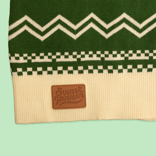 Grön stickad jultröja med vitt mönster och en läderpatch med Svenskhusman-logotyp på mudden.