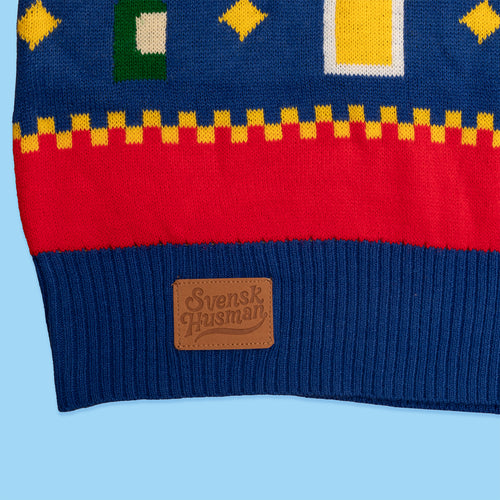 Detalj på blå stickad jultröja med julölstema och läderpatch med Svenskhusman-logotyp vid mudden.