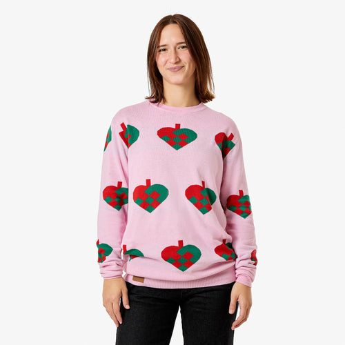 Rosa stickad jultröja med mönster av flätade röda och gröna julhjärtan på en person.