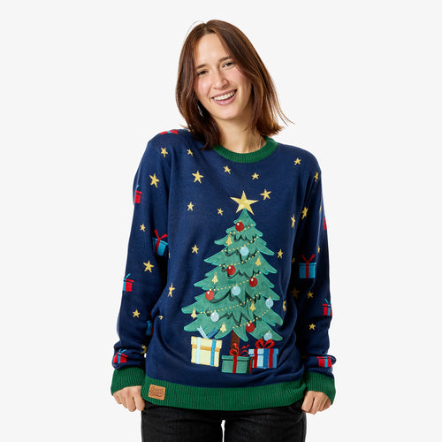 Mörkblå jultröja för dam med julgran, stjärnor och paket från Svenskhusman på en leende person mot vit bakgrund.