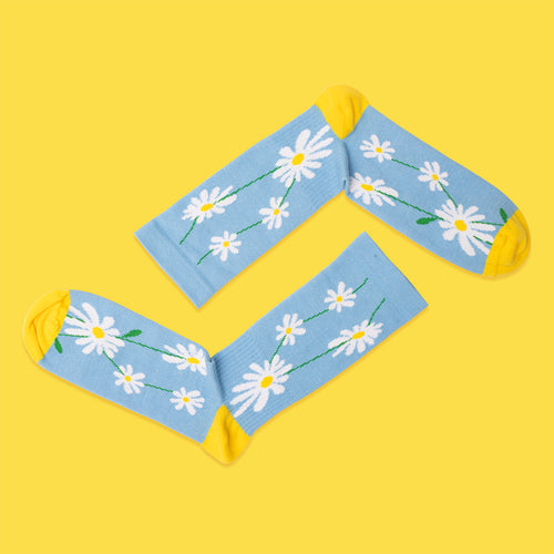 Light blue compression socks featuring white daisies and yellow accents on a vibrant yellow background.