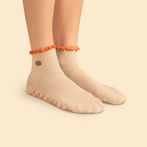 Beige pilatesstrumpor med halkskydd och dammsugarmotiv samt orange vågig kant på fötterna från Svenskhusman.