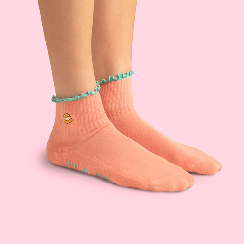 Beige pilatesstrumpor med semla-motiv och grön vågig kant på en person mot rosa bakgrund.