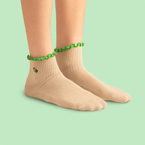 Beiga sneakersstrumpor med grön volangkant på fötterna mot ljusgrön bakgrund från Svenskhusman.