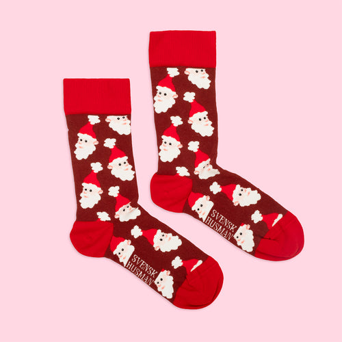Bruna julstrumpor med mönster av tomteansikten och röda detaljer från Svenskhusman på rosa bakgrund.