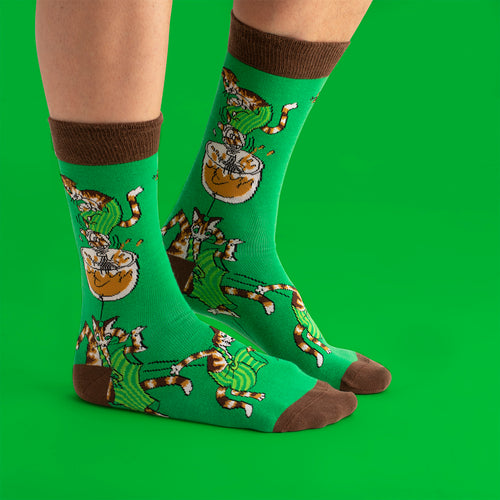 Gröna strumpor med motiv av Findus som vispar och bruna detaljer från Svenskhusman på grön bakgrund.
