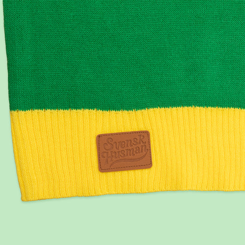 Detalj på grön och gul jultröja med Svenskhusmans logotyp på en brun läderlapp.