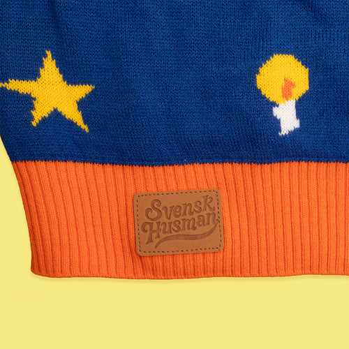 Blå stickad jultröja med orange mudd, läderlapp med logotyp samt motiv av stjärna och ljus från Svenskhusman.