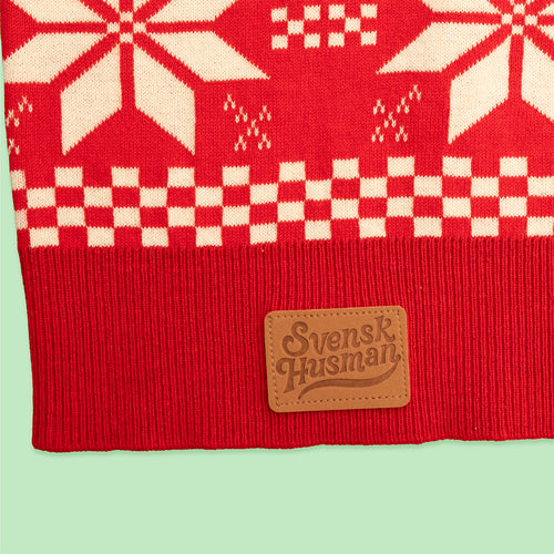 Stickad röd jultröja med vita snöflingor och rutigt mönster samt logotyp på läderlapp från Svenskhusman.