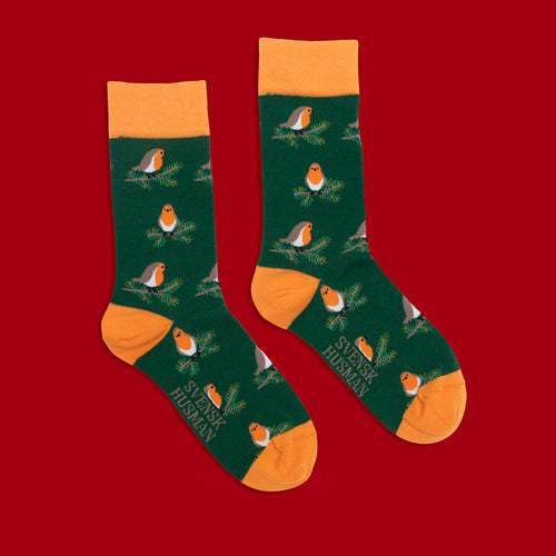 Grüna Socken med mönster av rothakar på grenar och orange detaljer från Schwedischhusman på rot bakgrund.