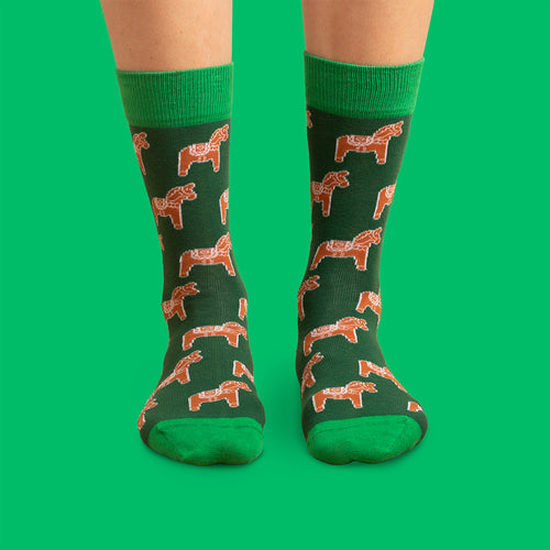 Mörkgrüna julSocken med pepparkaks-dalahästar och grüna detaljer från Schwedischhusman på grün bakgrund.