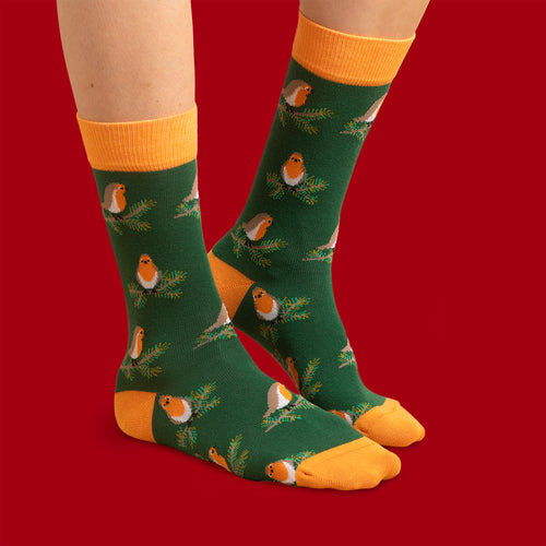 Mörkgrüna Socken med rothakar på grankvistar och orangea detaljer från Schwedischhusman på rot bakgrund.