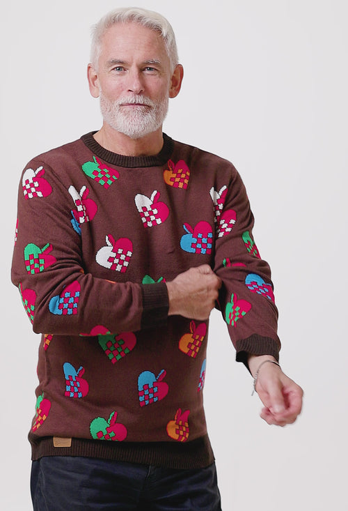 Manlig modell iförd en brun jultröja med färgglada julhjärtan från Svenskhusman framför en vit bakgrund.