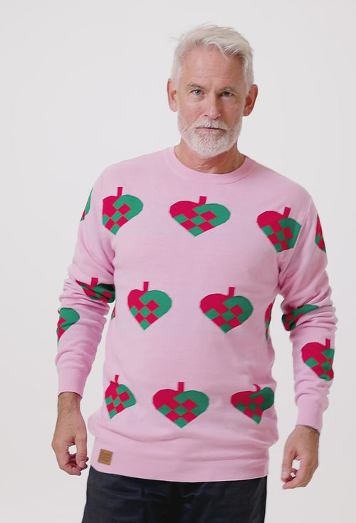 Man i rosa stickad jultröja med gröna och röda julhjärtan från Svenskhusman mot vit bakgrund.
