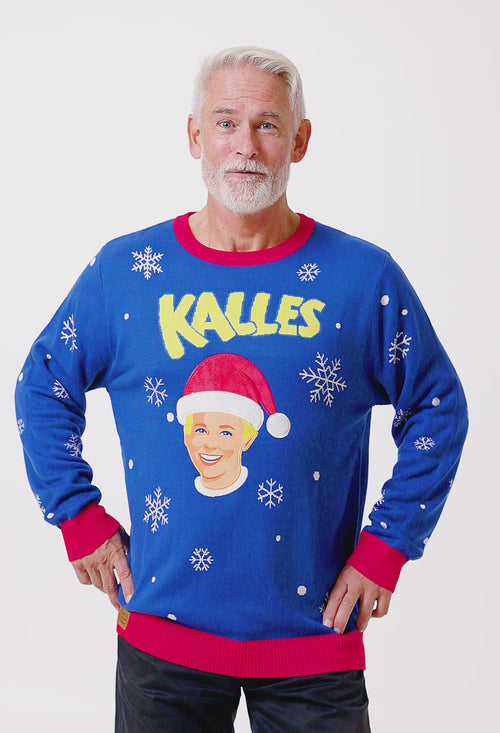 Blå stickad jultröja för herr med Kalles Kaviar-motiv, tomteluva och snöflingor på en modell.