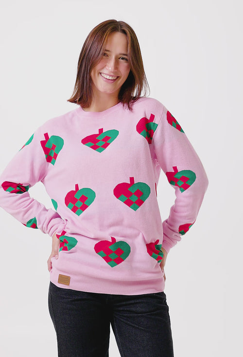 Rosa stickad jultröja med mönster av flätade julhjärtan i rött och grönt på en person från Svenskhusman.