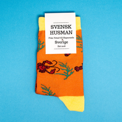 Orange Kindersocken von Svenskhusman mit roten Krebsen und Dillzweigen auf blauem Hintergrund.